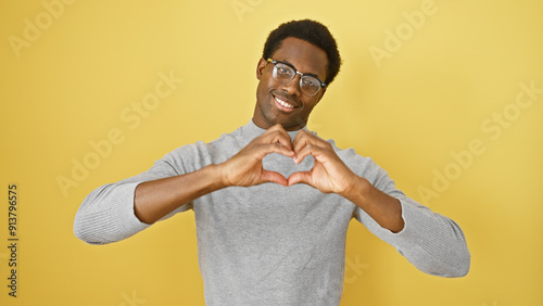 A smiling young african american man making a heart sign against a yellow isolated background. photo