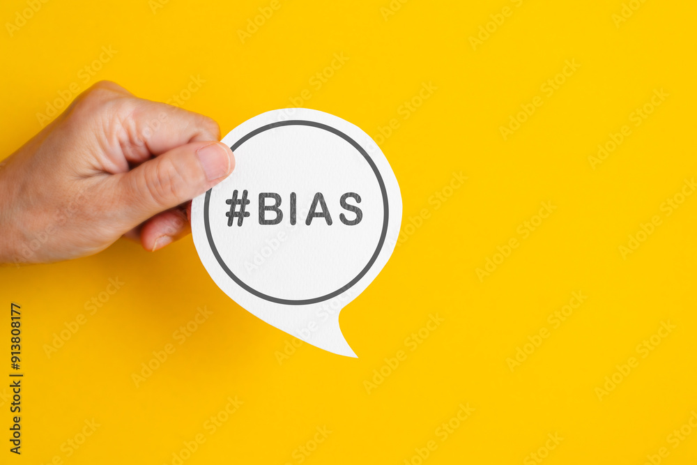 Hand holding real white speech bubble paper cut with BIAS word on yellow background Hand holding real white speech bubble paper cut with BIAS word on yellow background
