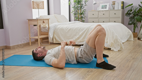 A young hispanic man relaxes on a yoga mat in a tidy bedroom, embodying tranquility and domestic lifestyle.