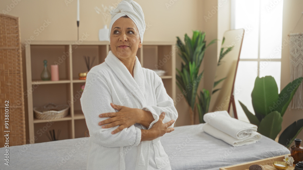Hispanic woman with crossed arms wearing a white robe in a serene spa room, surrounded by wellness decor and natural light. Hispanic woman with crossed arms wearing a white robe in a serene spa room, surrounded by wellness decor and natural light.