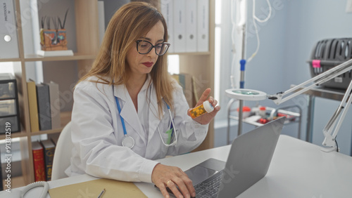 Woman working indoors at veterinary clinic holding medication bottle while using laptop