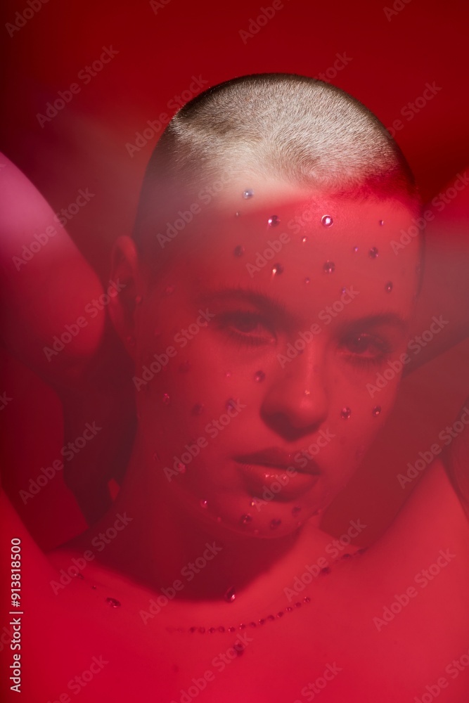 Distorted closeup portrait of bald young woman with crystal makeup looking at camera in red haze Distorted closeup portrait of bald young woman with crystal makeup looking at camera in red haze