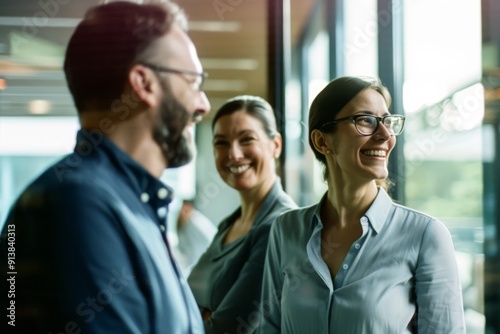 Three colleagues smiling and conversing, captured in a candid moment in a bright, modern office space.