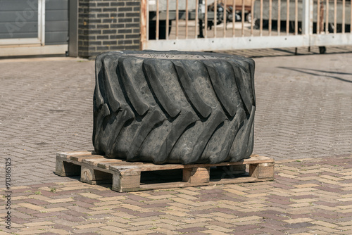 huge black rubber tire of a tractor lies outside on a wooden industrial pallet photo