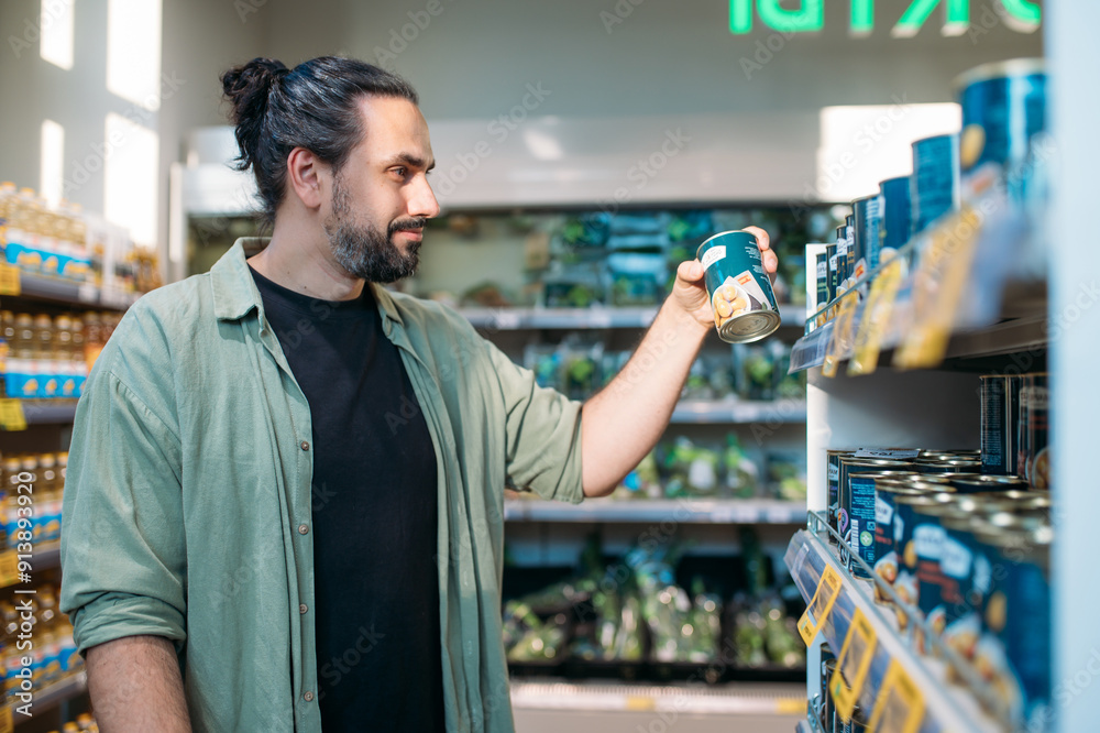 A young man is shopping at the supermarket. The guy picks canned food from the counter in the store A young man is shopping at the supermarket. The guy picks canned food from the counter in the store