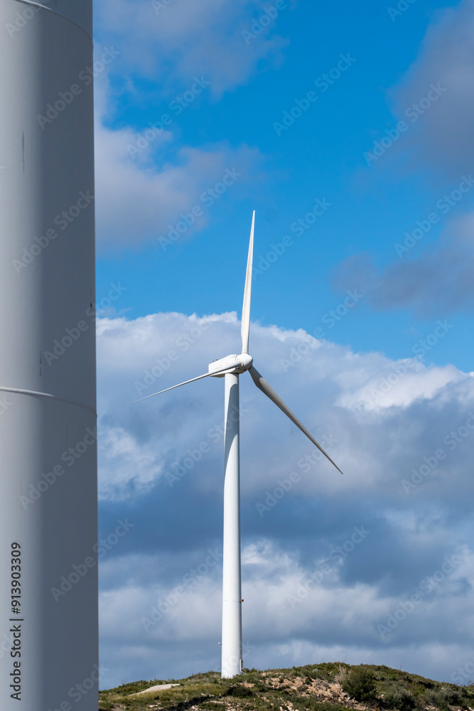 A lone wind turbine stands tall against a strikingly blue sky dotted with white clouds, signifying solitude, strength, and the harnessing of natural energy resources in Tarragona Spain A lone wind turbine stands tall against a strikingly blue sky dotted with white clouds, signifying solitude, strength, and the harnessing of natural energy resources in Tarragona Spain