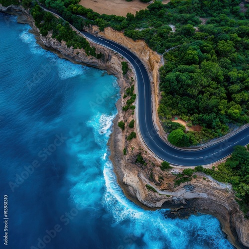 Aerial view of a winding coastal road alongside vibrant blue ocean and lush greenery, offering a scenic route perfect for travel.