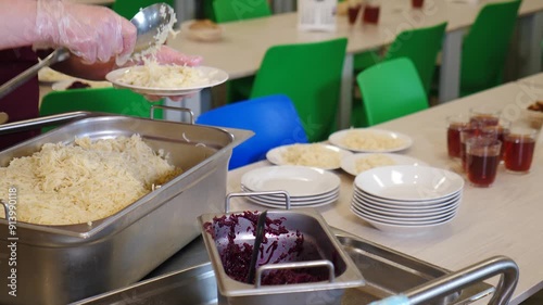 Canteen worker serving dishes on plates for students in modern school cafeteria. Modern canteen, cafe, restaurant of public catering. Different dishes on distribution zone in dining room. School