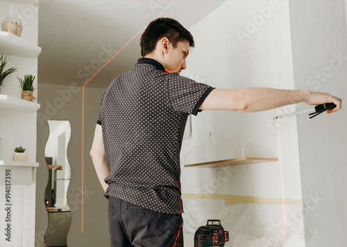 A young man checks the levelness of a shelf with a laser level. photo