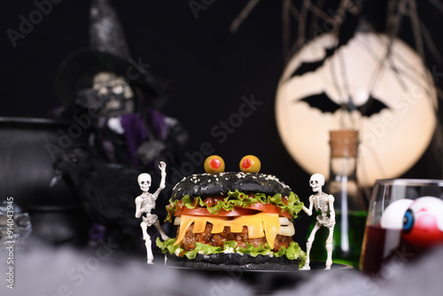 Monster Burger. Black bun, juicy beef cutlet, lettuce, onion, tomato and cheese in the shape of teeth, in the company of skeletons. Definitely a pick-me-up and a perfect Halloween party appetizer photo