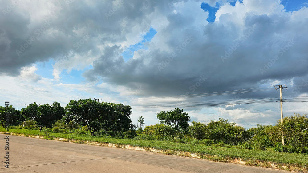 Dark storm clouds loom over a rural road flanked by lush greenery and trees Dark storm clouds loom over a rural road flanked by lush greenery and trees