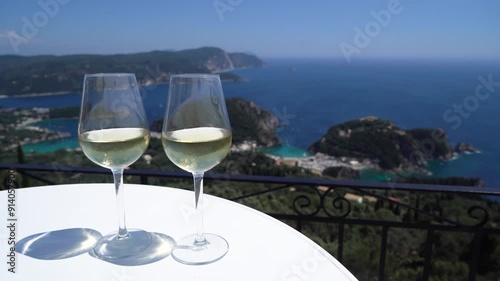 Pouing white wine intoglasses with Corfu seascape in background photo