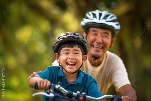 A joyful young boy rides his bicycle with his grandfather in a park, both wearing helmets and smiling brightly. The background features lush greenery, cheerful and lively scene.