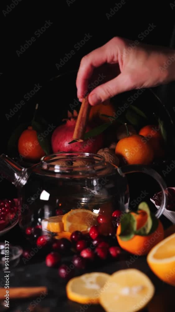 A hand gently places orange slices into a glass teapot for a warm winter beverage A hand gently places orange slices into a glass teapot for a warm winter beverage