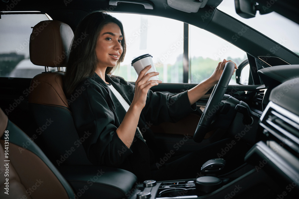 White cup of fresh drink in hand. Beautiful businesswoman is in the new car