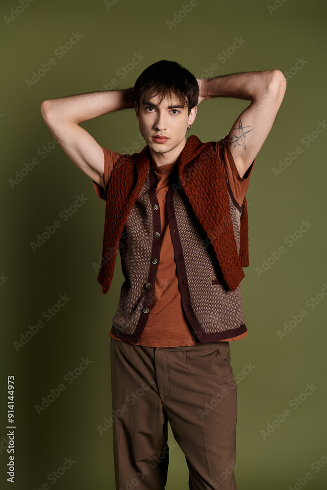 A stylish man in a knitted vest and brown pants poses against a green backdrop. A stylish man in a knitted vest and brown pants poses against a green backdrop.