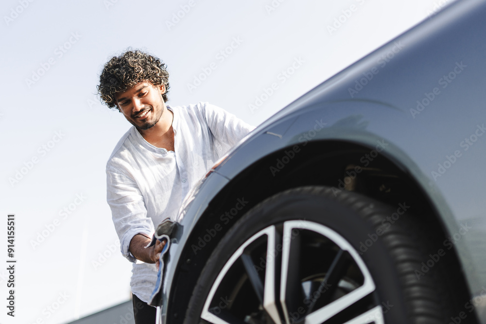 Smiling Indian man cleaning his modern electric car with microfiber cloth Smiling Indian man cleaning his modern electric car with microfiber cloth