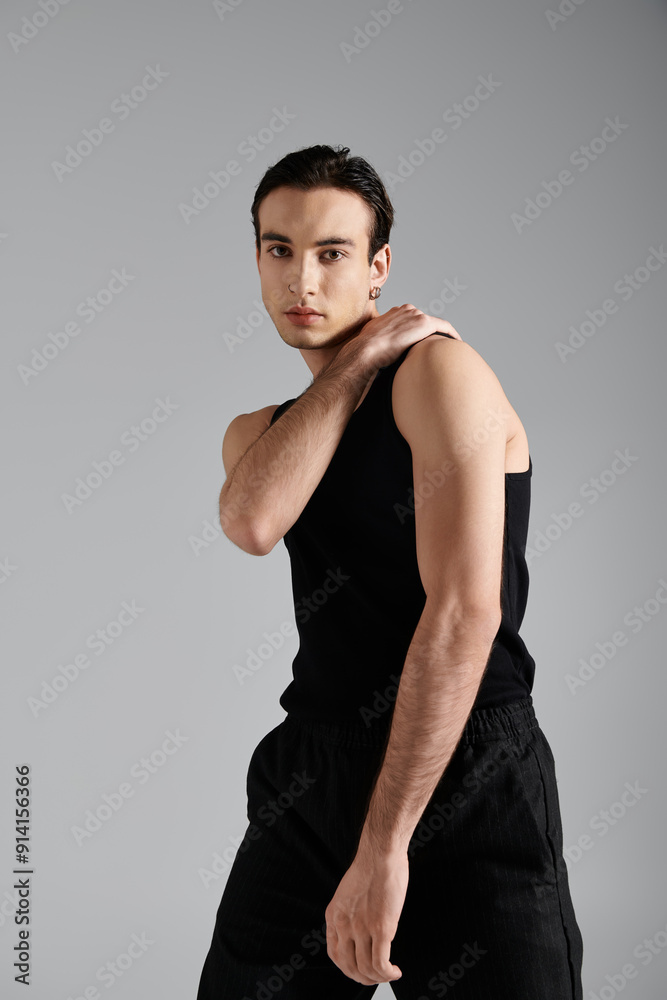 A handsome man in a black tank top poses against a grey background. A handsome man in a black tank top poses against a grey background.