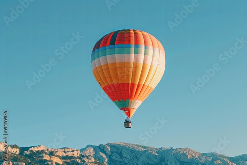 Colorful hot air balloon flying over mountains against a blue sky.