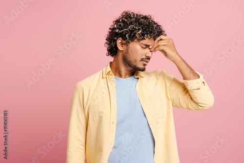 Young Indian man suffering from headache touching his temples on pink background