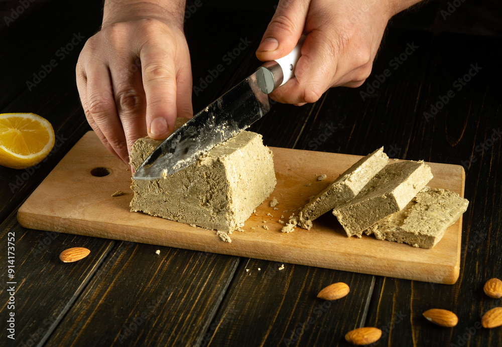 Sunflower halva is cut with a knife before serving the dessert on the table. The knife in the man hand cuts a piece of halva. Sunflower halva is cut with a knife before serving the dessert on the table. The knife in the man hand cuts a piece of halva.
