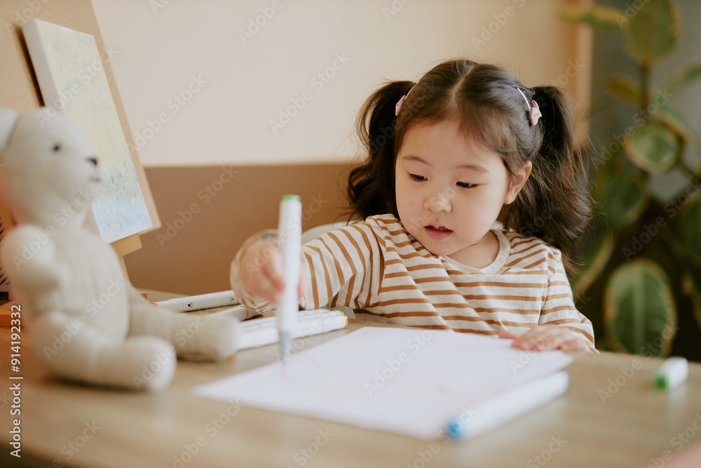Focused Asian girl with two ponytails drawing at desk with help of felt-tip pens Focused Asian girl with two ponytails drawing at desk with help of felt-tip pens