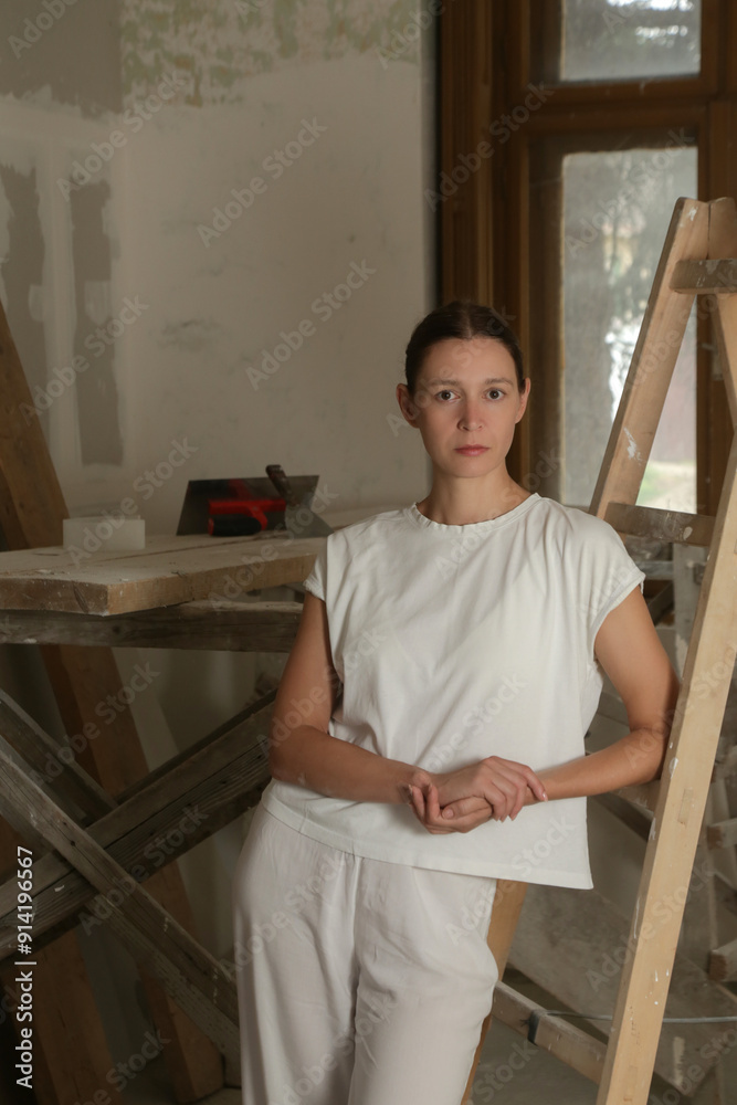 Portrait of a young woman leaning on the ladders during renovation DIY concept, fixing wall surface and preparation for painting. Portrait of a young woman leaning on the ladders during renovation DIY concept, fixing wall surface and preparation for painting.