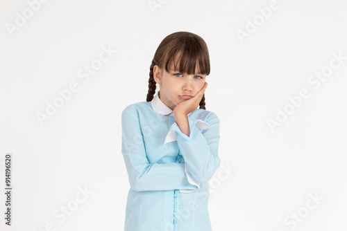 Cute school girl standing in uniform, holding palm on cheek and leaning face on it, being bored and tired of uninteresting talks, feeling indifferent to what happening over white wall