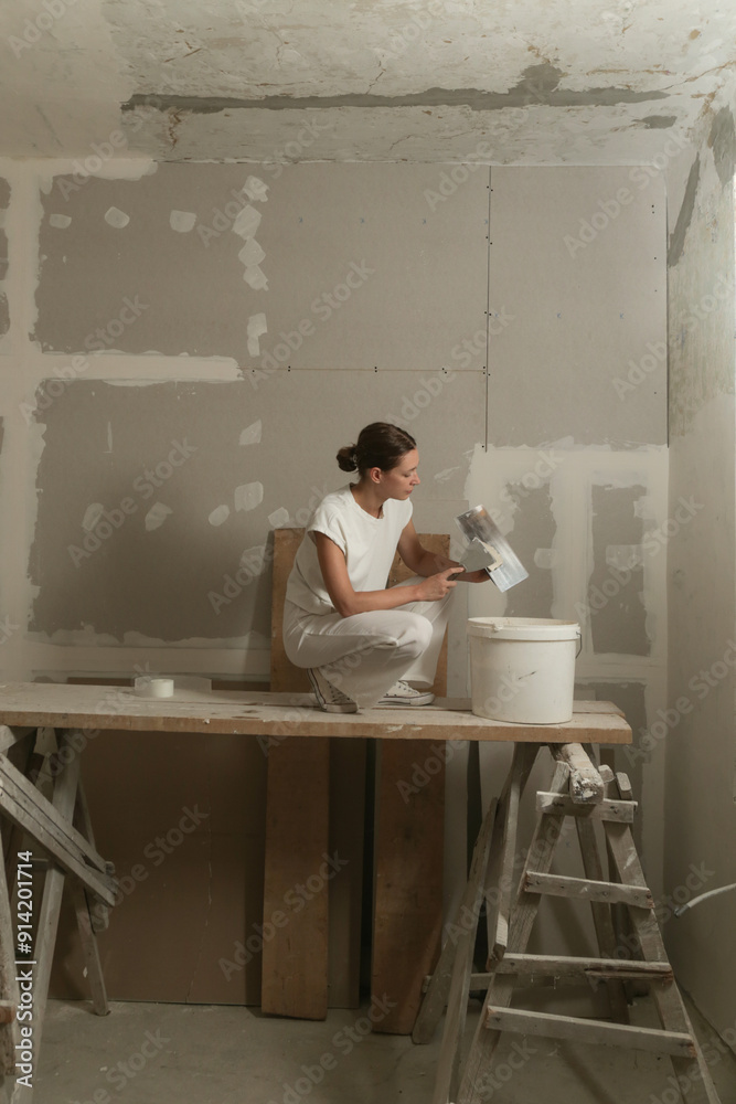 Woman taping and mudding joins pieces of drywall into a single solid wall. Fixing dry wall surface and preparation for painting. DIY housing improvement project. Woman taping and mudding joins pieces of drywall into a single solid wall. Fixing dry wall surface and preparation for painting. DIY housing improvement project.