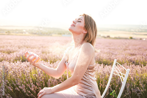 Young glamorous woman with a bottle of perfume in a lavender field