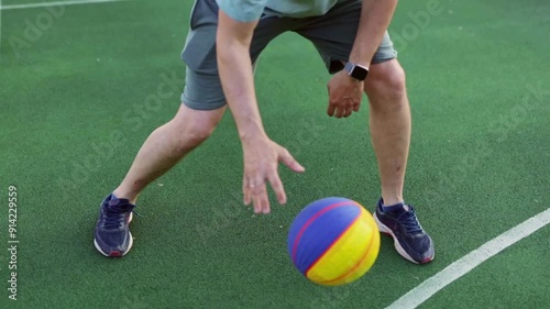 Dynamic young man dunking basketball at center of green court. Active man dressed in blue t-shirt engaging in outdoors training plays basketball On the Sunset. Concept of workout and exercising.