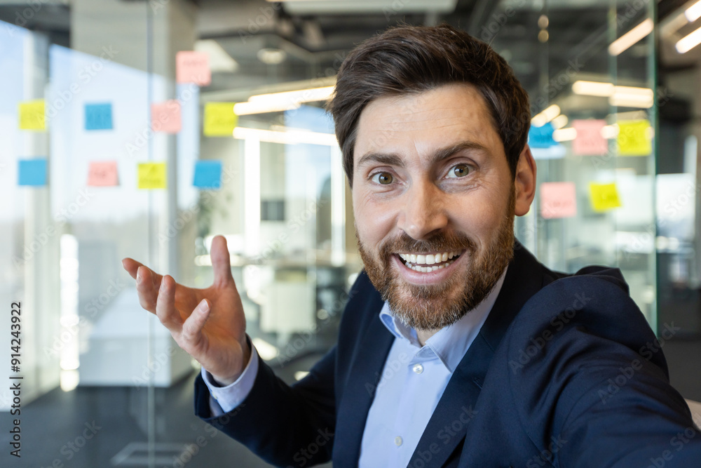 Confident businessman smiling and making gesture while on video call using phone in modern office. Professional dressed in suit enjoying virtual meeting with colleagues or clients. Confident businessman smiling and making gesture while on video call using phone in modern office. Professional dressed in suit enjoying virtual meeting with colleagues or clients.