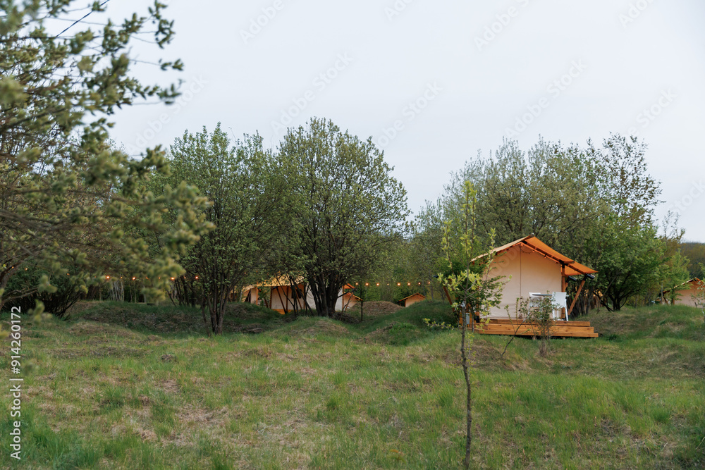 Cozy open glamping tents with light inside in summer camp. Camping tent for holiday and vacation