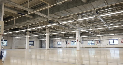 Dolly shot of an old, closed down large factory floor or hall. Large empty industrial space, ceiling mounted lighting, real time, no people