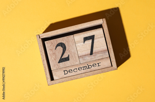 Wooden block calendar with the date december 27 on yellow background photo