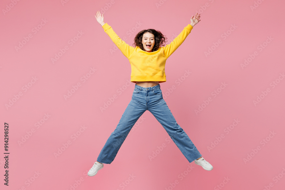 Full body young surprised fun excited woman wearing yellow sweatshirt casual clothes jump high jump high spread hands isolated on plain pastel light pink background studio portrait. Lifestyle concept. Full body young surprised fun excited woman wearing yellow sweatshirt casual clothes jump high jump high spread hands isolated on plain pastel light pink background studio portrait. Lifestyle concept.