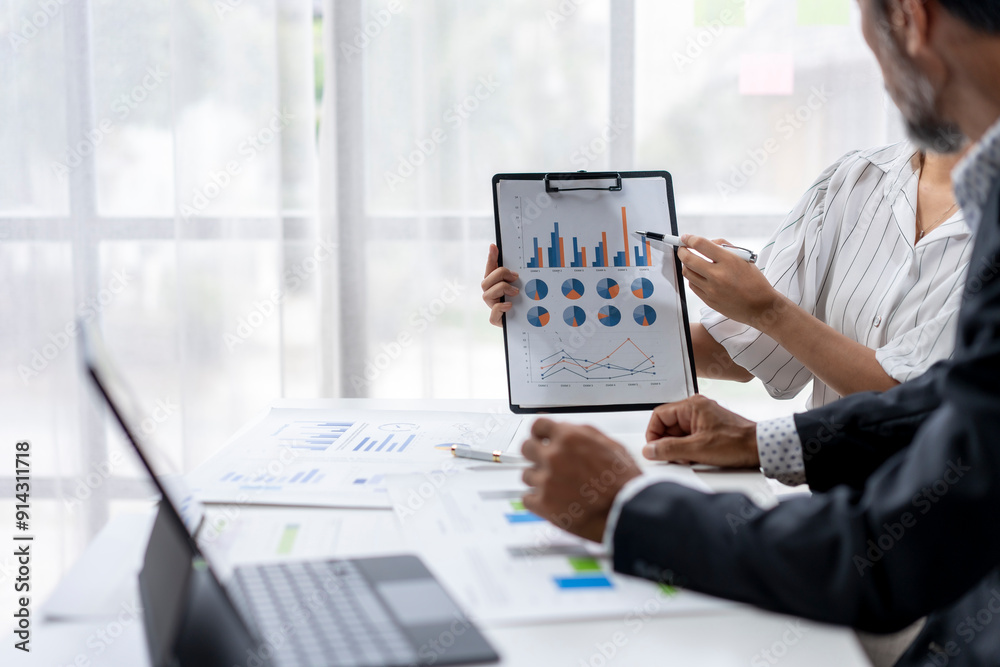 Two people are looking at a presentation with graphs on a table Two people are looking at a presentation with graphs on a table