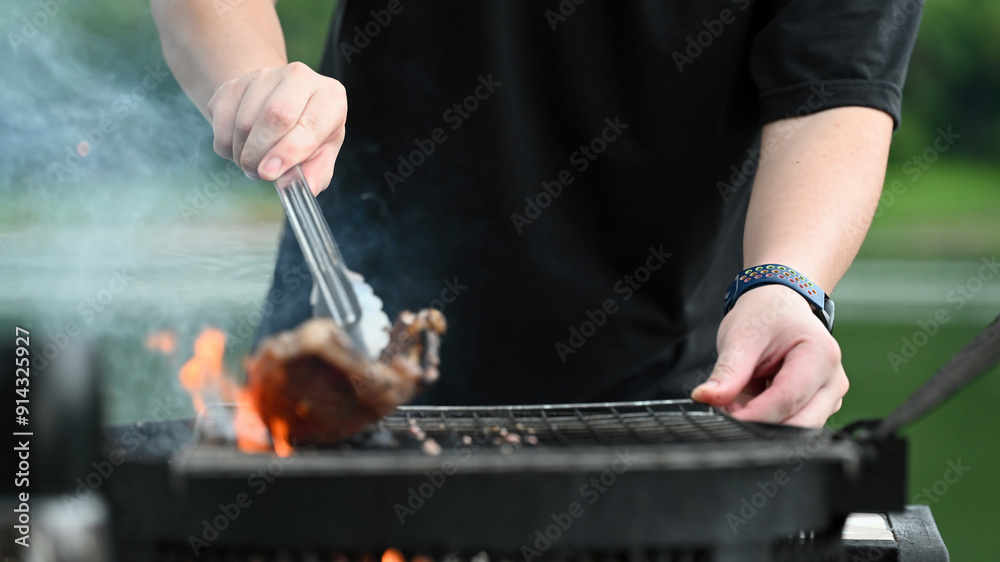 A person using tongs to lift a steak off the grill, with flames and smoke creating a dramatic backdrop, capturing the skill of grilling outdoors A person using tongs to lift a steak off the grill, with flames and smoke creating a dramatic backdrop, capturing the skill of grilling outdoors