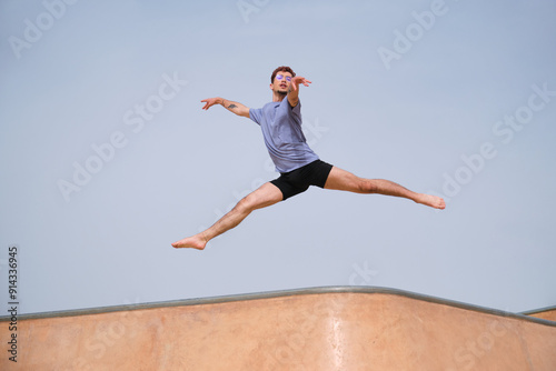 Obraz na płótnie Dancer is performing a split jump over a skatepark ramp against a clear blue sky w salonie