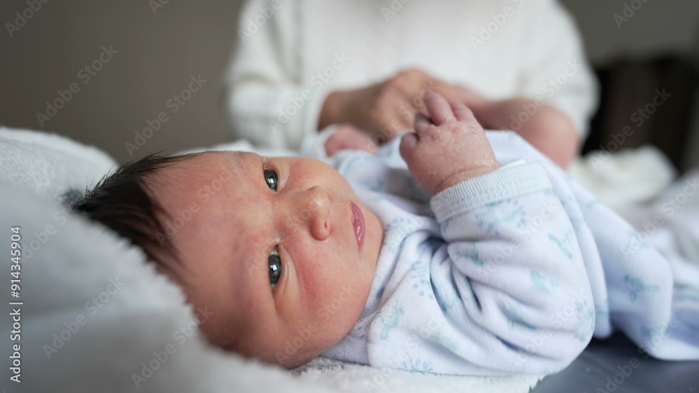 Newborn baby looking up while grandmother puts on clothes after diaper change, tender and nurturing moment, family bonding, cozy home environment, multi-generational love Newborn baby looking up while grandmother puts on clothes after diaper change, tender and nurturing moment, family bonding, cozy home environment, multi-generational love
