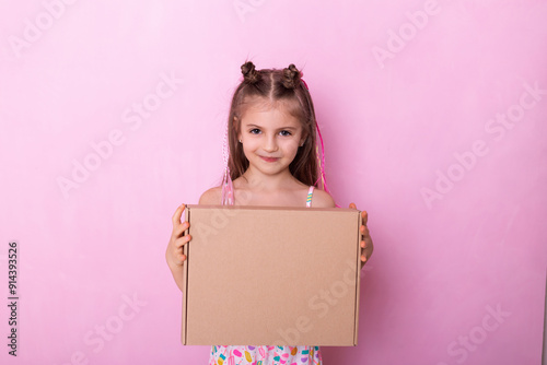 Girl holding a box on pink background.  Beautiful childe with cardboard box in hands. A little girl holding big cardboard box isolated on pink.