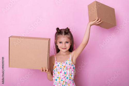 Smiling little girl with many cardboard boxes.  Girl holding a boxes on pink background.  Beautiful childe with cardboard boxes in hands.