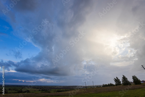 Dark clouds loom over rolling hills as twilight approaches, casting unique shadows and allowing soft beams of light to peek through the stormy sky.