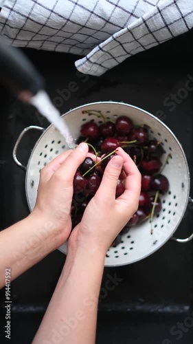 Woman washes ripe cherries in a black sink under running water. Vertical video of fresh cherries in a colander under running water. photo