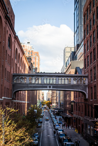 Photograph of a small, enclosed steel bridge with glass windows connecting two skyscrapers in New York City. The bridge serves as an elevated walkway, with a busy avenue and people visible below