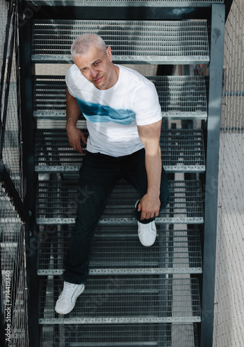 Fotografie A man in a white shirt and blue jeans is standing on a set of stairs