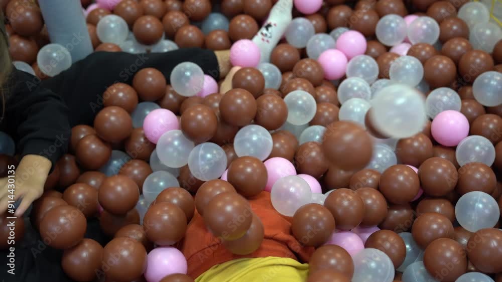 Two children play on colorful plastic balls in a large dry children's pool in the play center. They bury each other in balloons. Active leisure. High quality 4k footage Two children play on colorful plastic balls in a large dry children's pool in the play center. They bury each other in balloons. Active leisure. High quality 4k footage