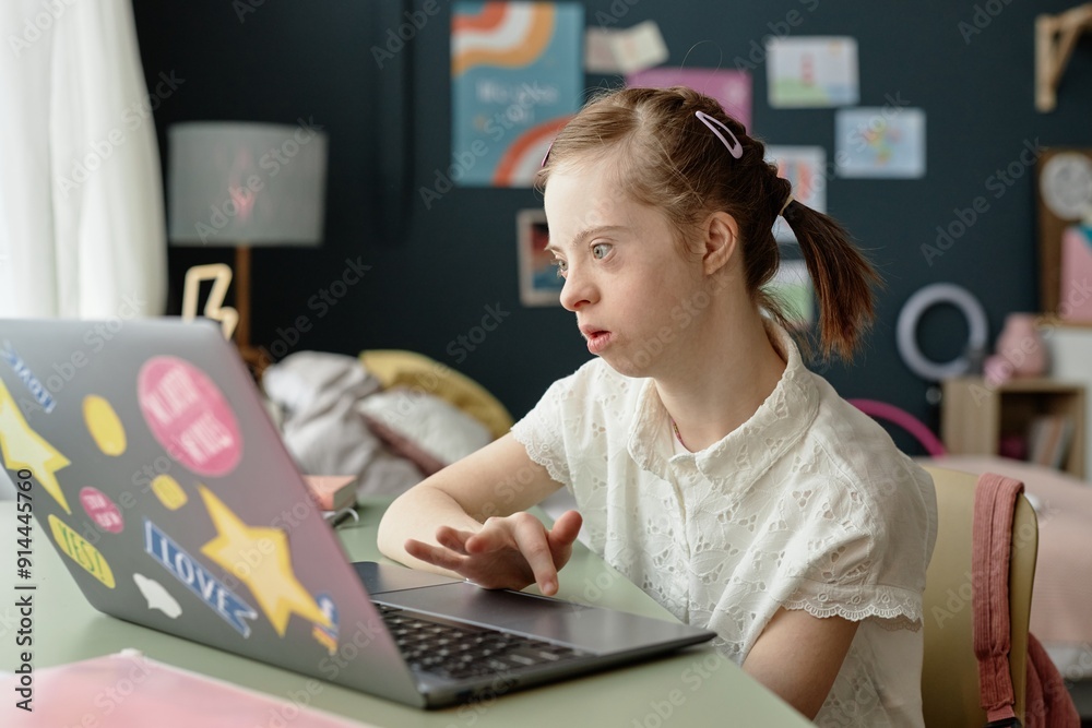 Girl using laptop in cozy room decorated with artwork and a lamp, focusing on screen and working diligently while sitting at desk with curtain letting in light without casting shadows Girl using laptop in cozy room decorated with artwork and a lamp, focusing on screen and working diligently while sitting at desk with curtain letting in light without casting shadows
