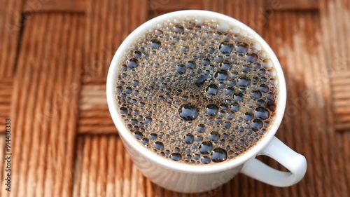 POV of someone pouring a cup of coffee. A cup of espresso. A close-up of a black coffee cup. Bubbles popping in a mug. A hot drink. Someone serving a hot beverage. Coffee drops.