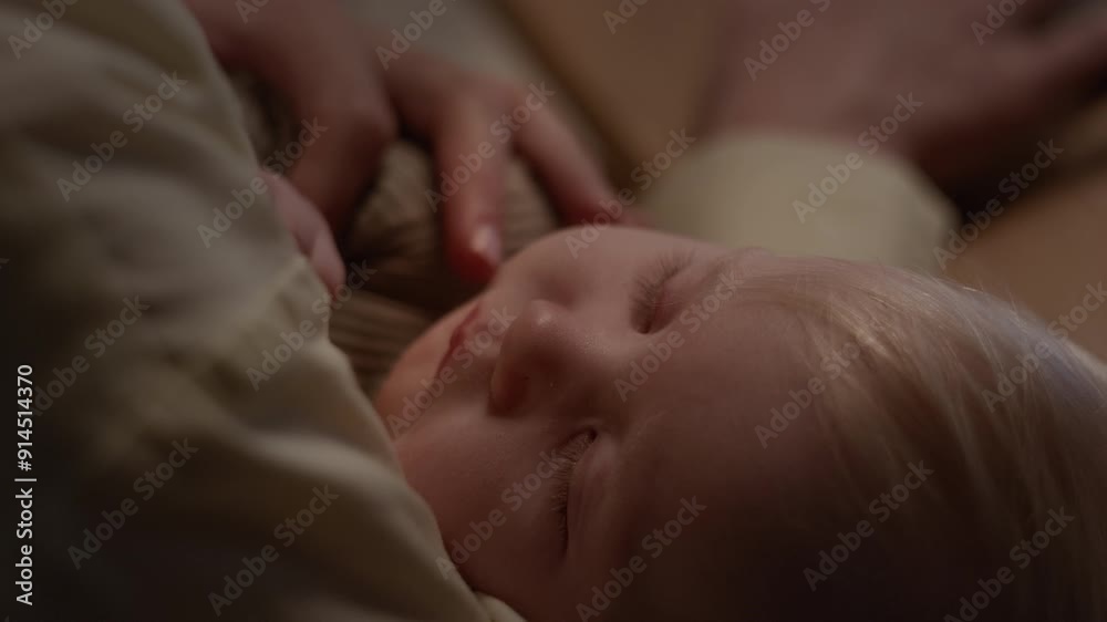Close-up of face of adorable Caucasian baby boy or girl with blond hair peacefully sleeping in arms of unrecognizable mother, feeling warmth and security Close-up of face of adorable Caucasian baby boy or girl with blond hair peacefully sleeping in arms of unrecognizable mother, feeling warmth and security